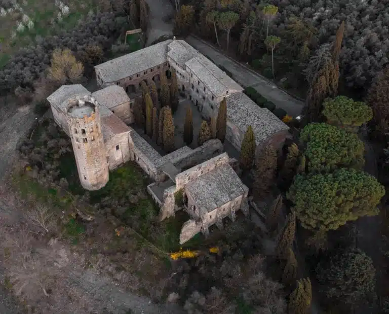 Aerial view of a historic stone castle with a round tower and walled cloister set among tall trees.