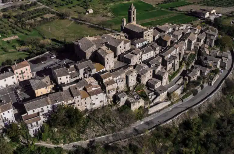 Aerial view of a stone hillside village with a central church tower and narrow winding streets.