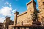 castello-bolsena – Orvieto | Orvietoviva Historic stone fortress with tall towers and crenellations against a bright blue sky; a griffin statue in the foreground.